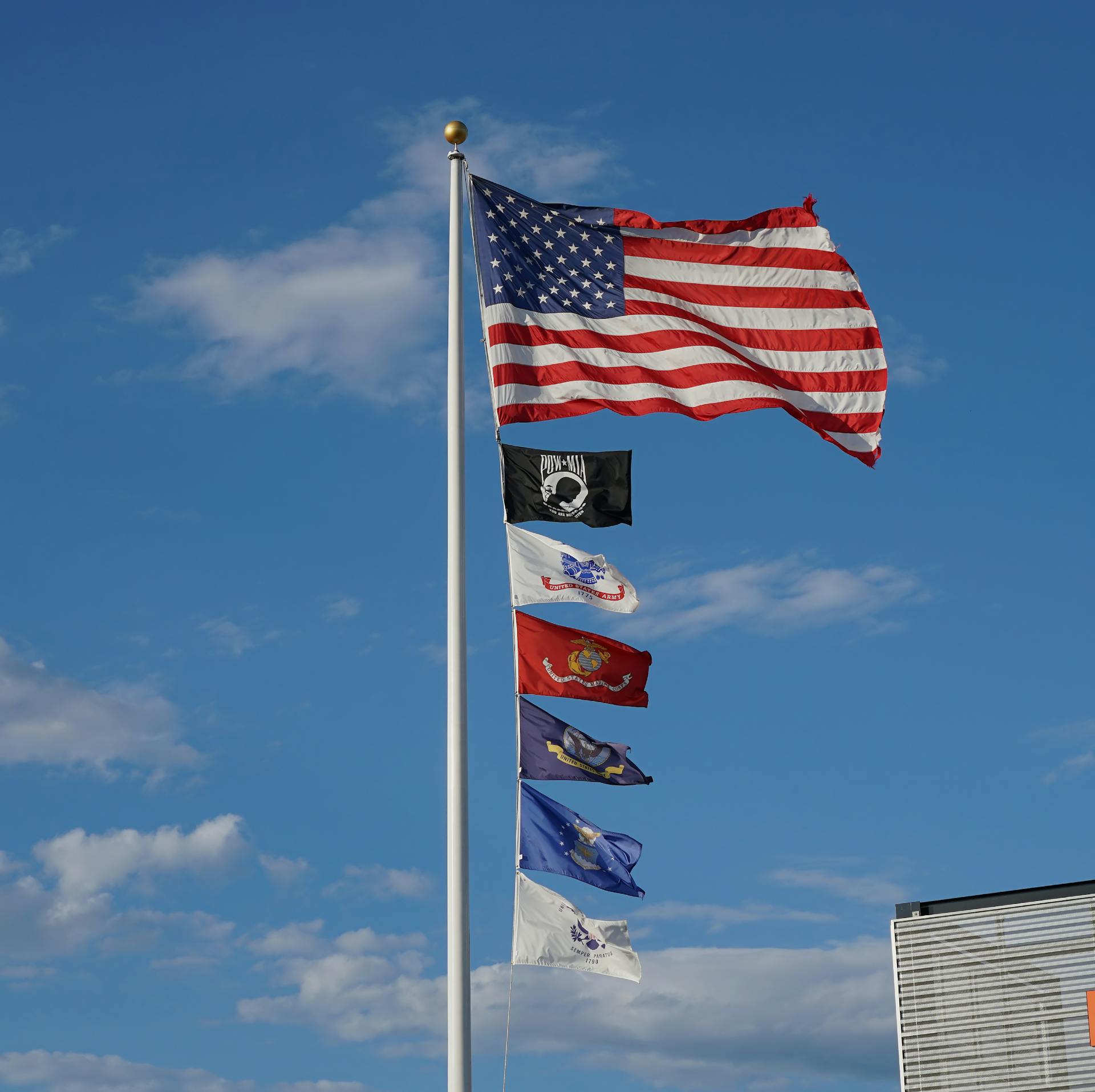 American flag and military service flags waving under a clear blue sky.