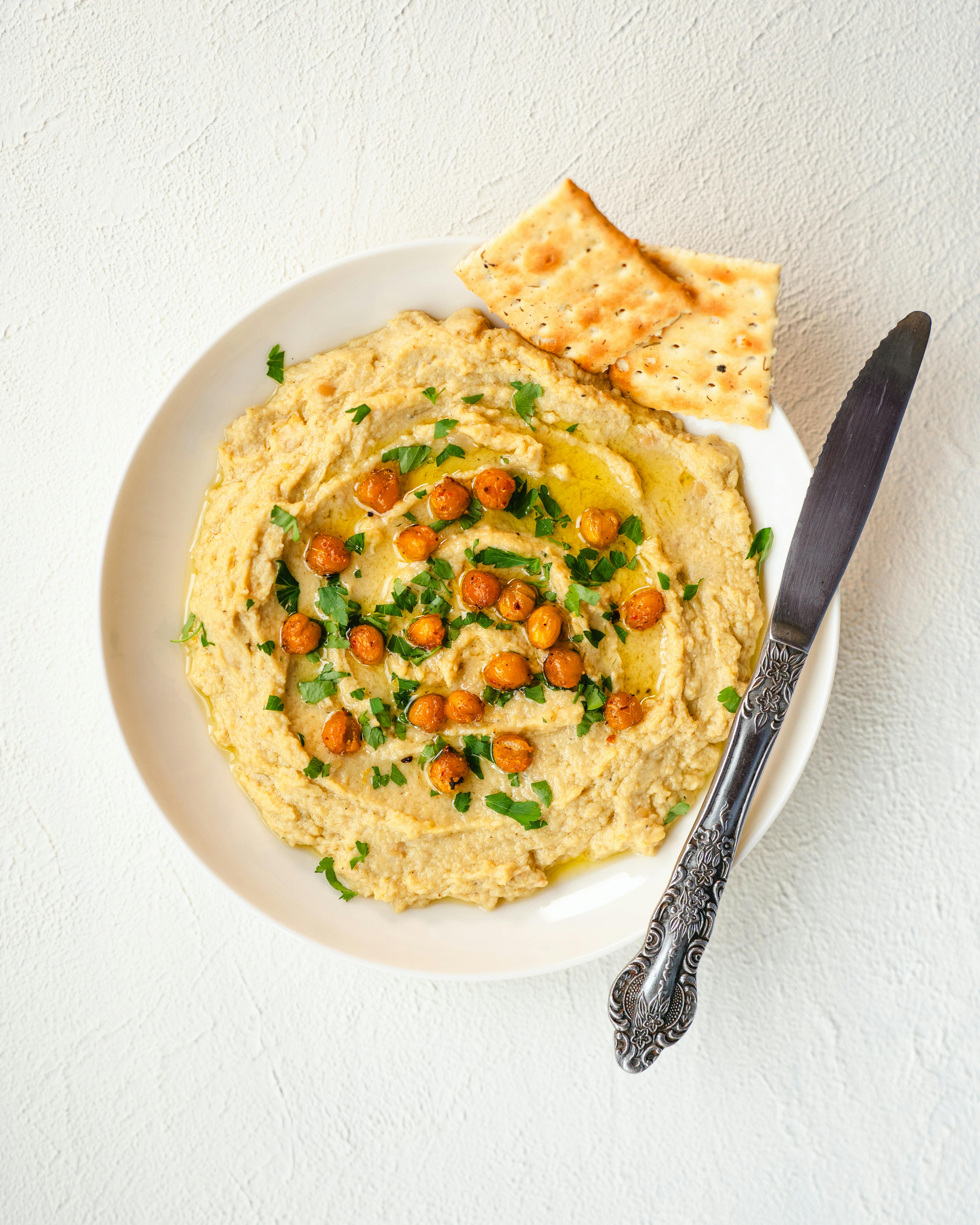 Flat lay of creamy hummus garnished with chickpeas and herbs, served with crackers.