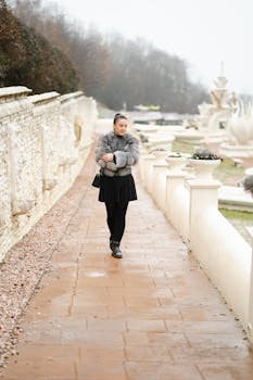 Elegant woman in fur coat and black dress walking along a scenic path.