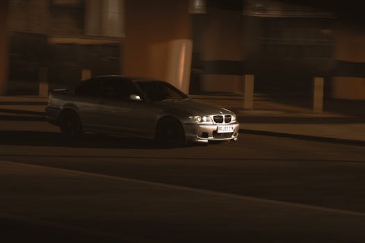 A silver car speeds through city streets at night, capturing motion and urban energy.