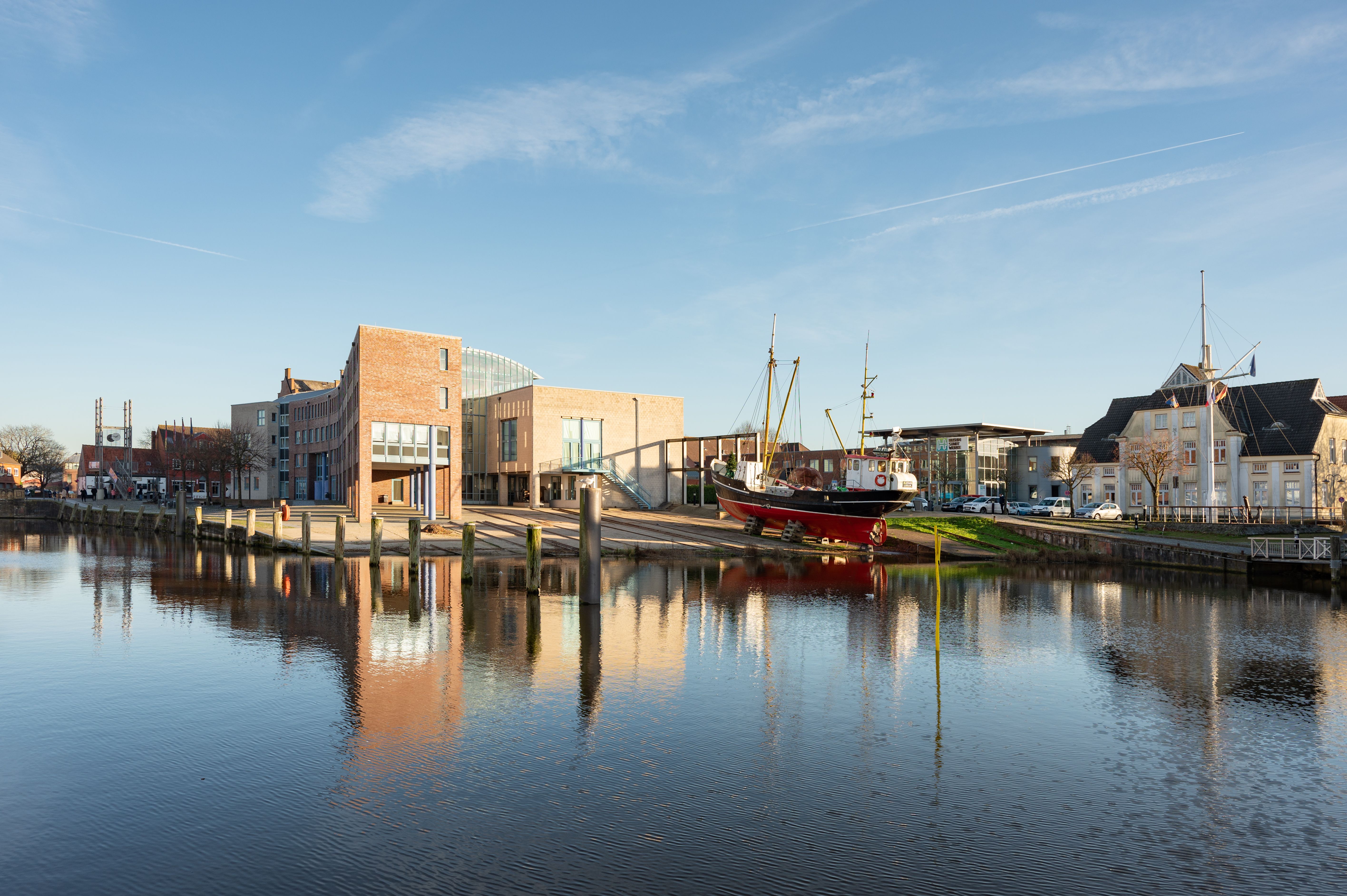 Beautiful scene of Husum harbour with ships and buildings reflected in the water.