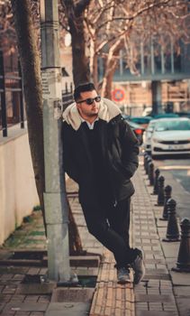 Casually dressed man in urban setting leaning against a streetlight