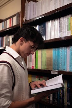 Stylish young man reading in an elegant library setting, surrounded by books.