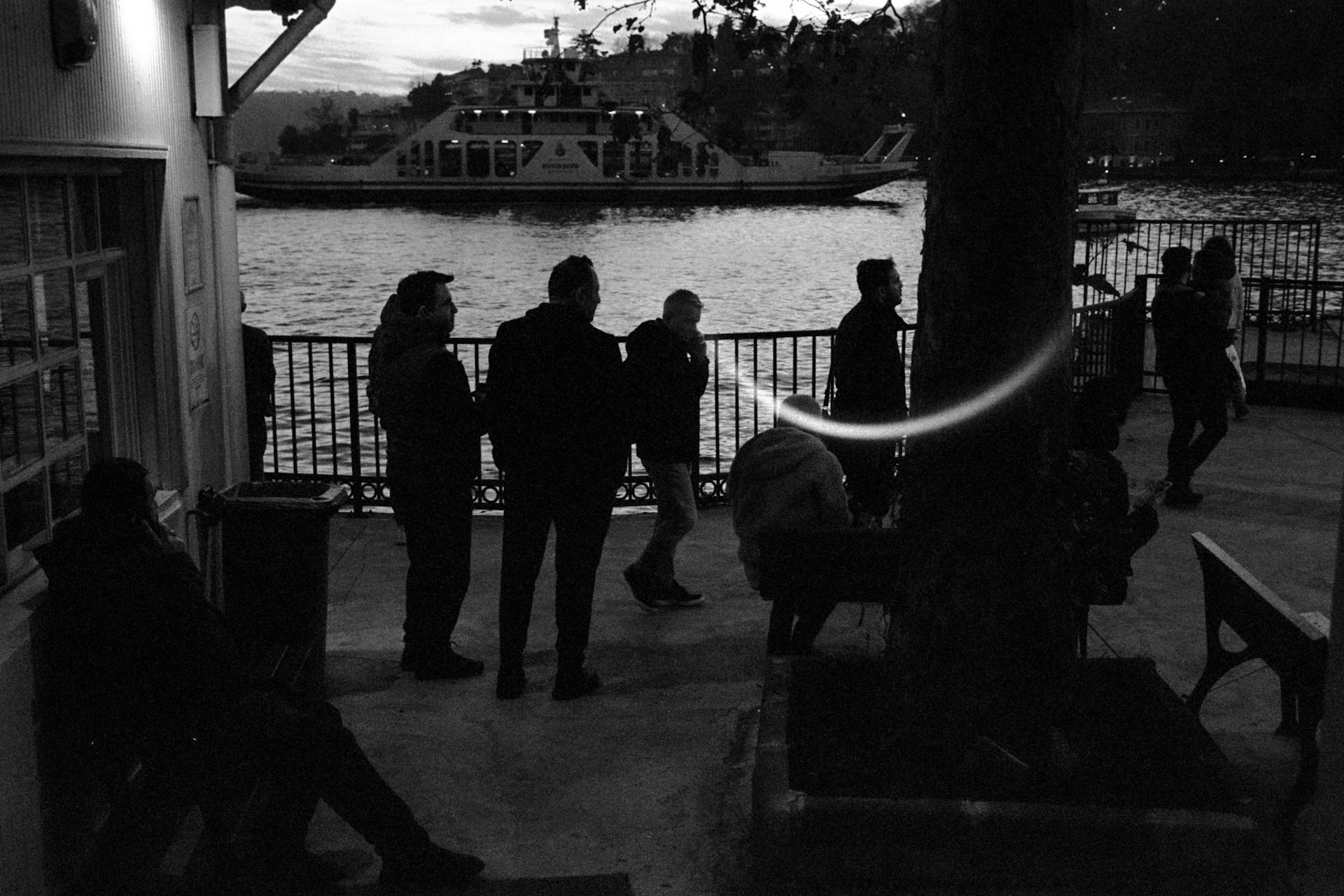 Silhouettes of people by the water in Istanbul with a ferry in the background.