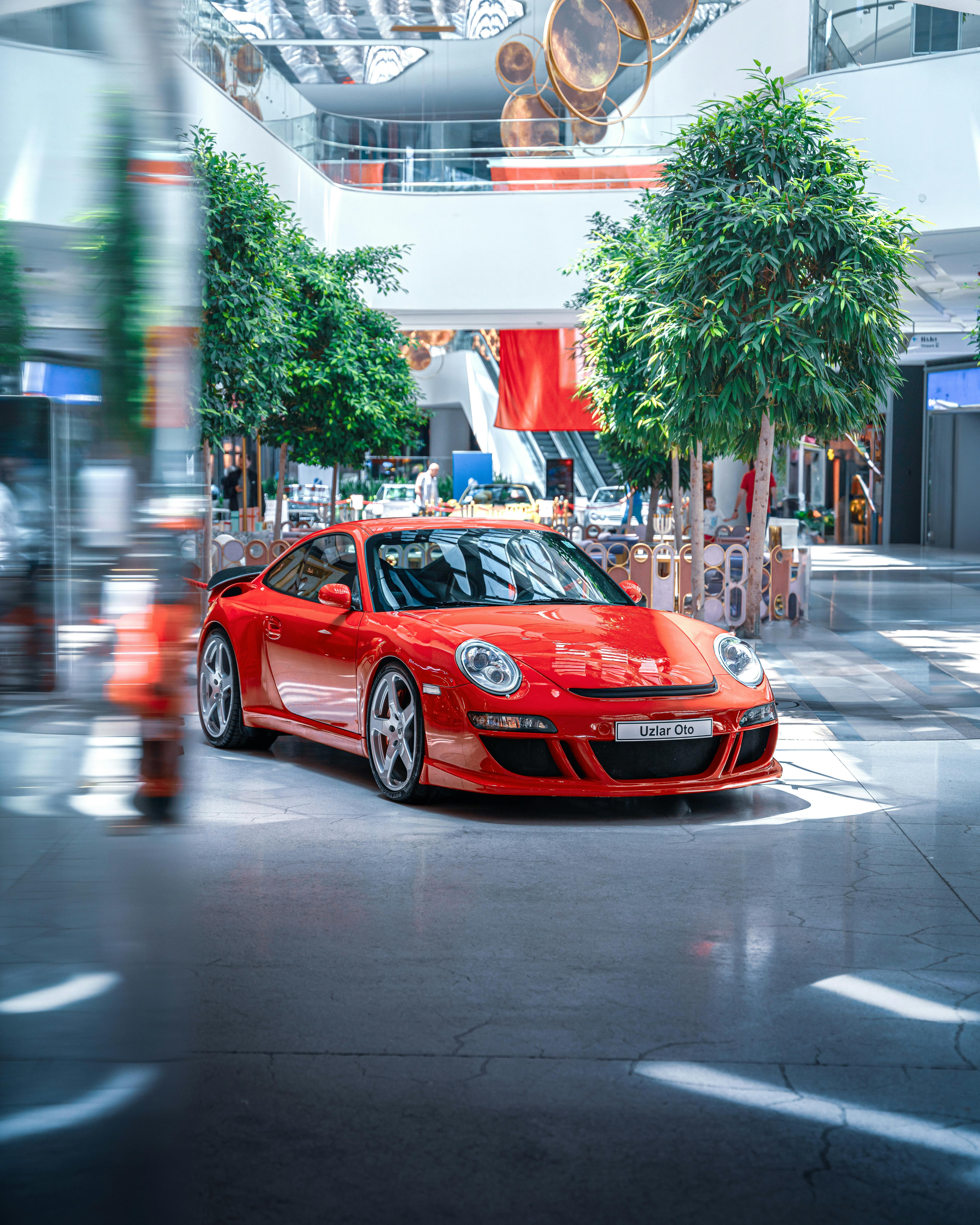 Vibrant red sports car displayed in a stylish modern mall atrium with lush greenery.