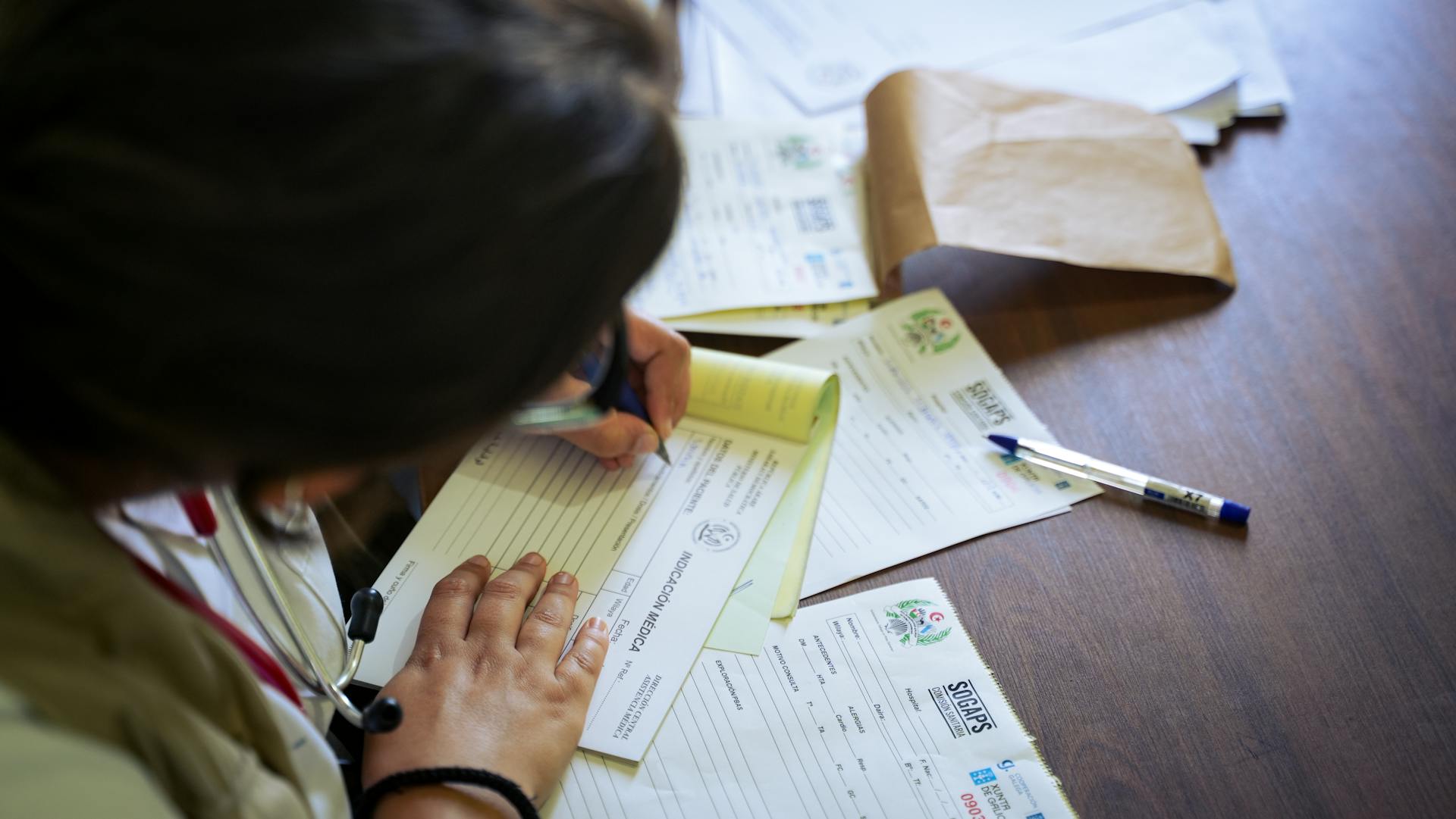 A doctor fills out medical forms indoors, focusing on patient care and documentation.