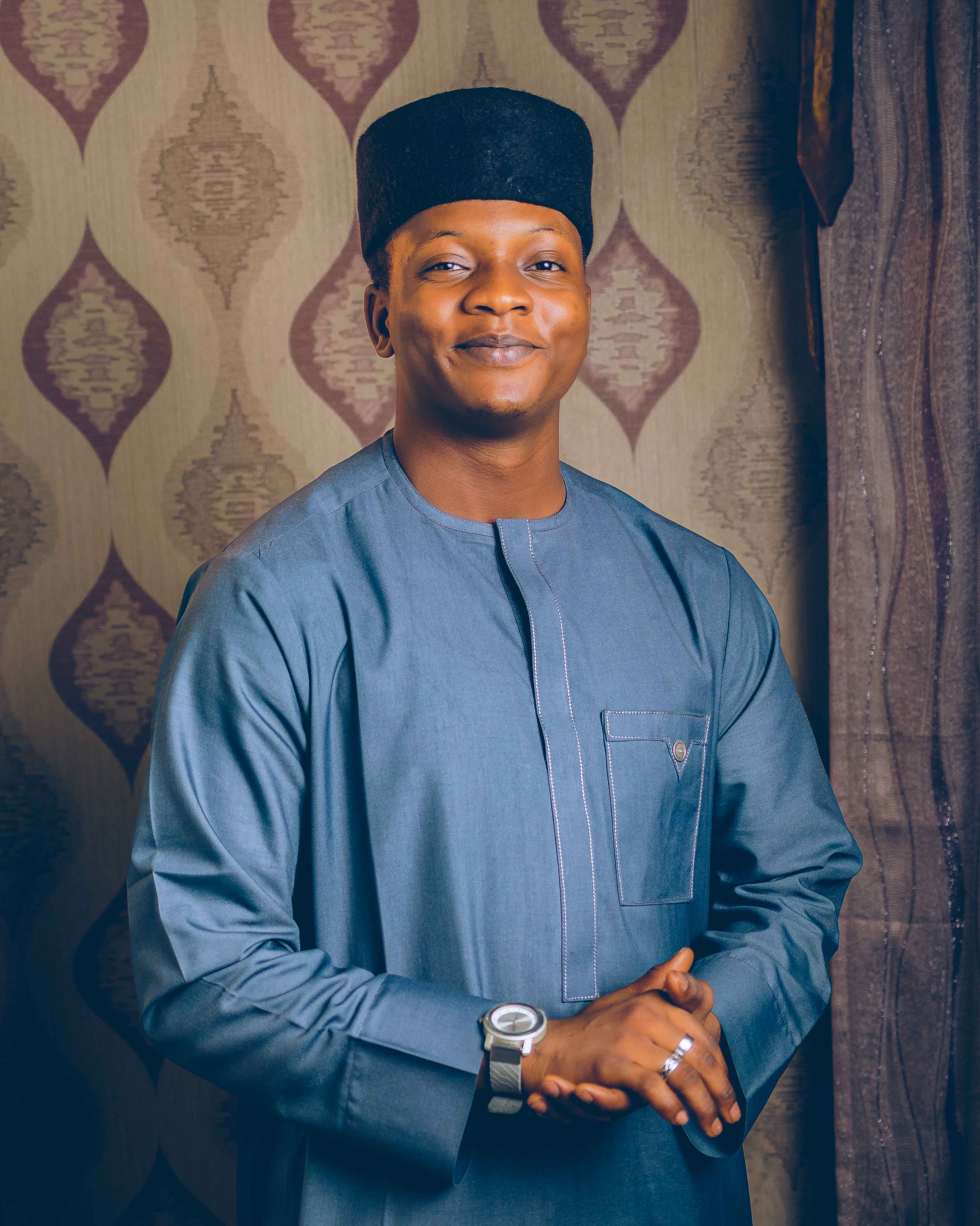 Smiling man in traditional attire with a patterned backdrop, showcasing cultural style.