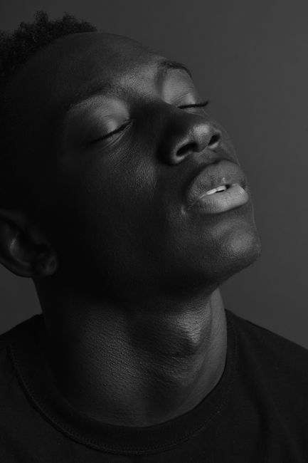 Emotive black and white portrait of a young man, eyes closed, in a studio setting.