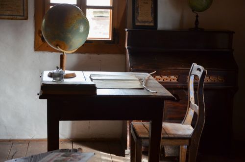 Free A nostalgic classroom setting featuring a globe, wooden desk, and piano with warm light. Stock Photo