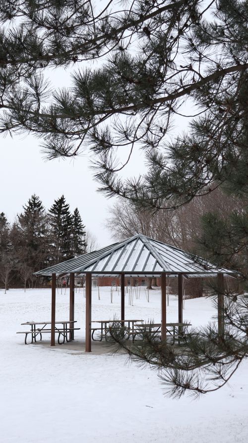 Free A tranquil winter scene featuring a gazebo in a snow-covered park, surrounded by trees. Stock Photo