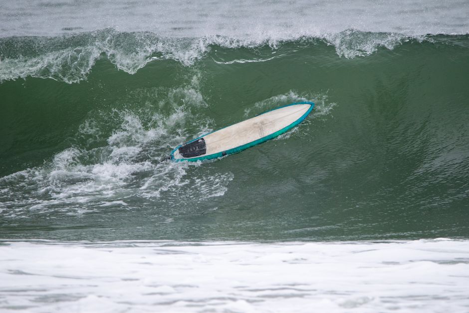 A lone surfboard navigates a vibrant green wave in Narragansett, Rhode Island, showcasing nature's power during winter.