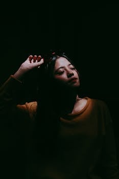 一幅室内艺术肖像中，一位亚洲女性摆着姿势，画面带有醒目的阴影和温暖的色调