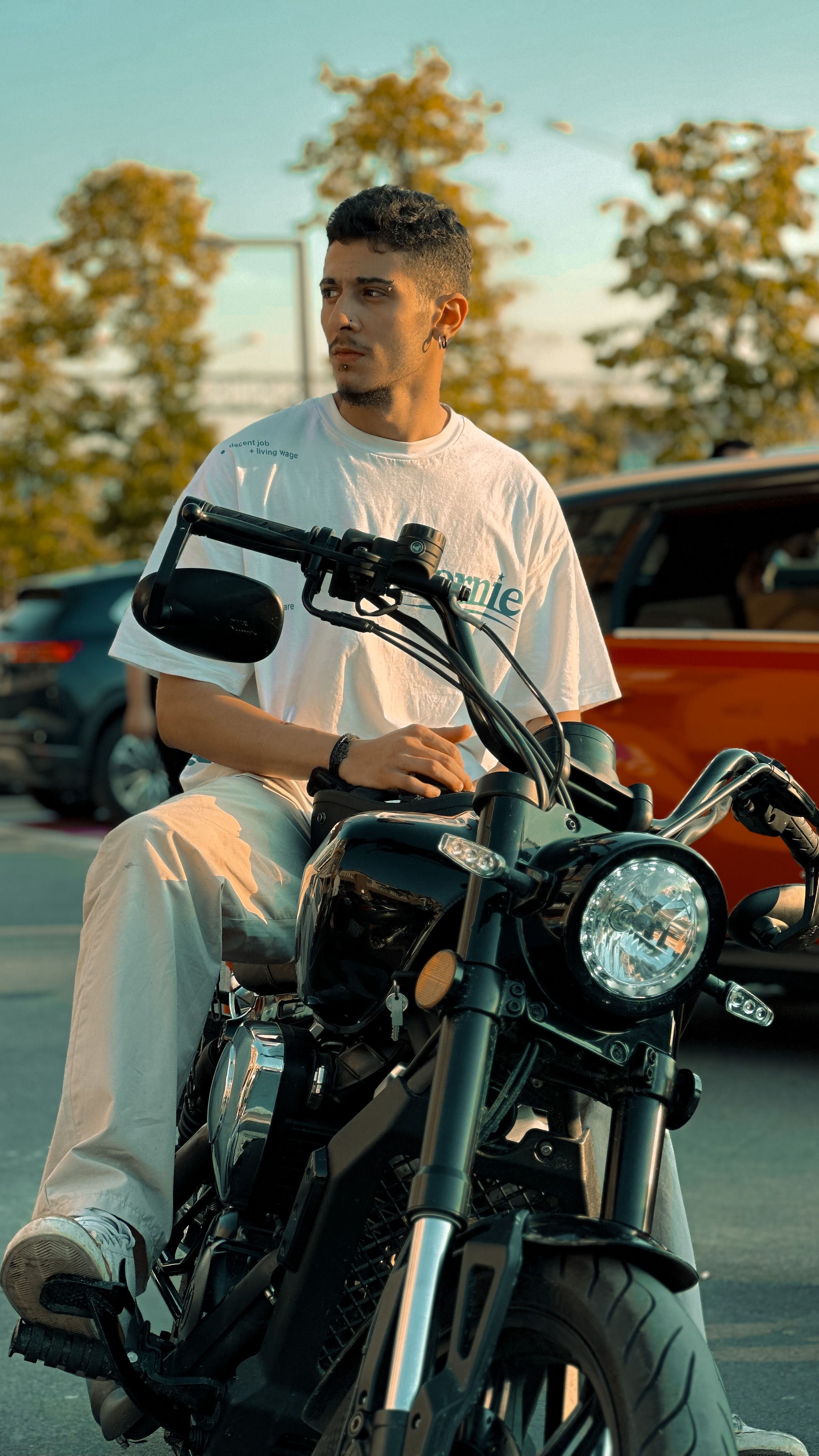 A young man sits on a motorcycle outdoors, exuding a cool and stylish vibe.