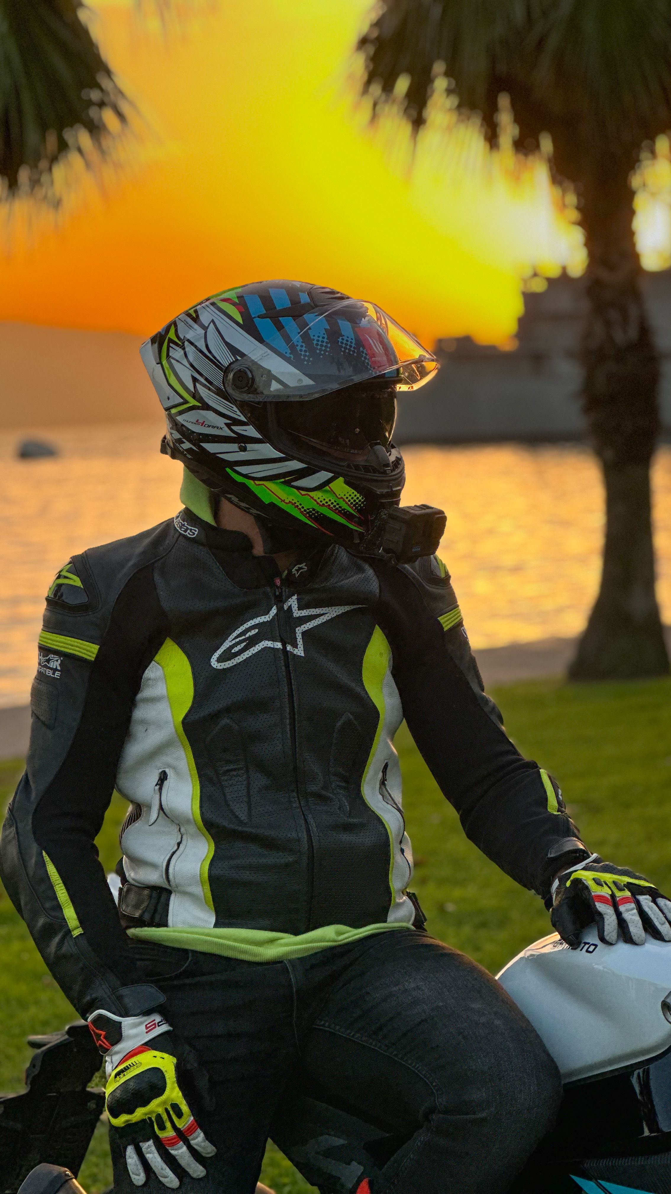 Motorcyclist in gear sitting by the sea at sunset, reflecting serene beauty.
