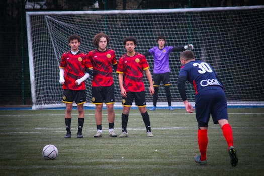 Soccer players setting up for a freekick on a grass field with goalkeeper ready.