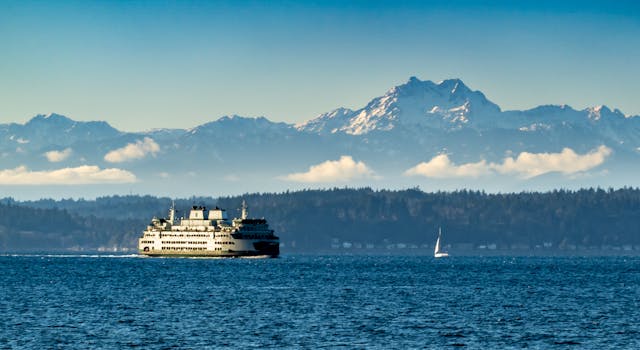 Seattle ferry crossing with Olympic Mountains in the background, blue sky, and ocean waves.
