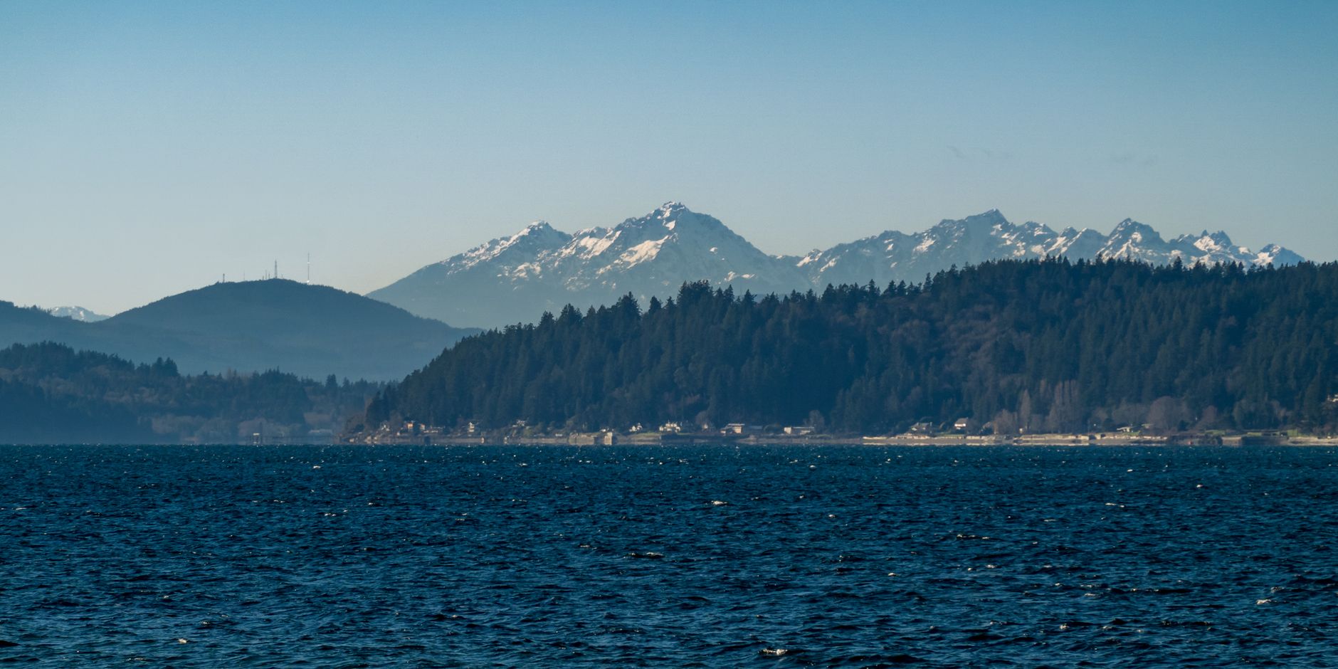 Calm waters and lush forests frame the majestic snow-capped Olympic Mountains in Seattle.