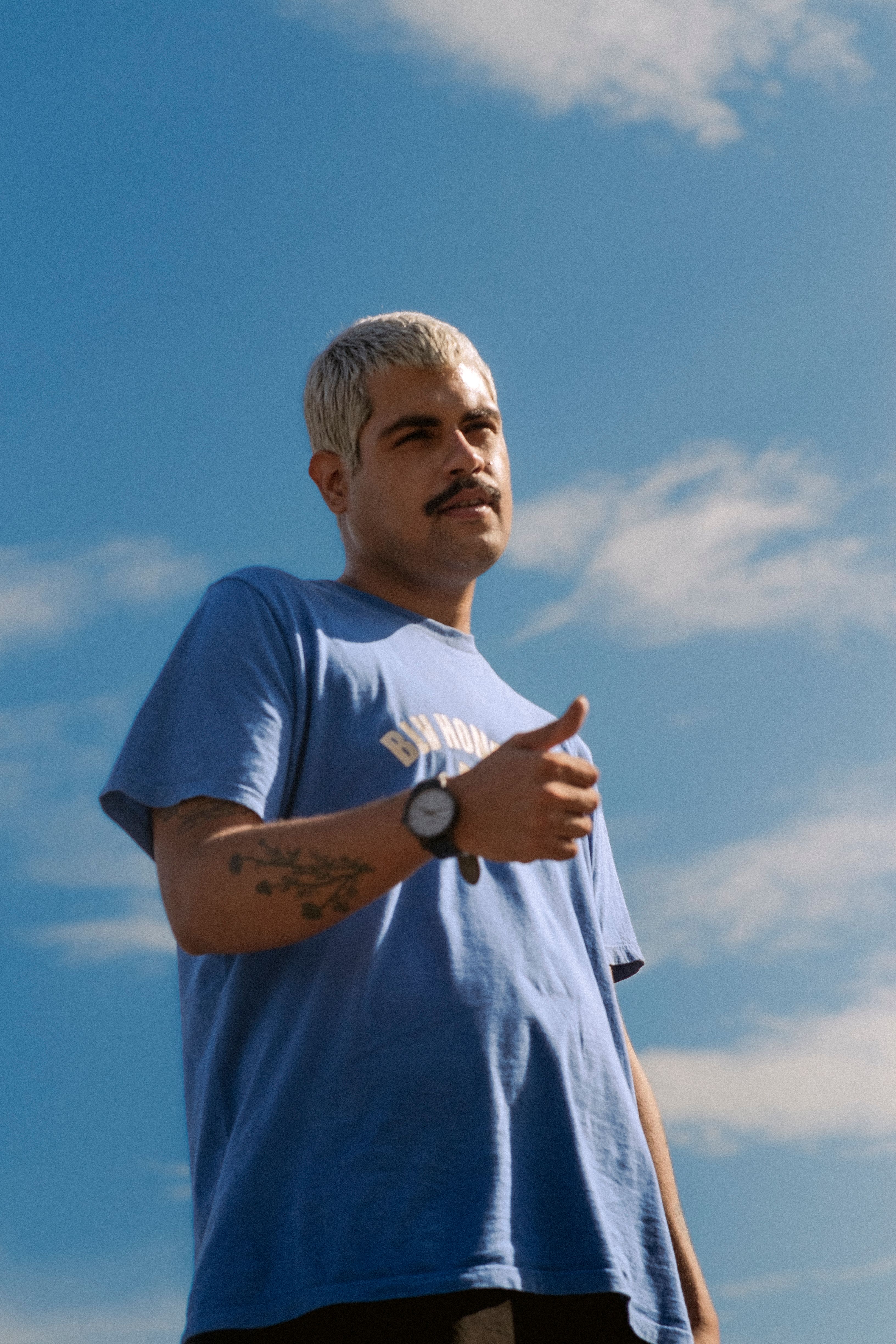 Man with tattoos giving a thumbs up gesture under clear sky.