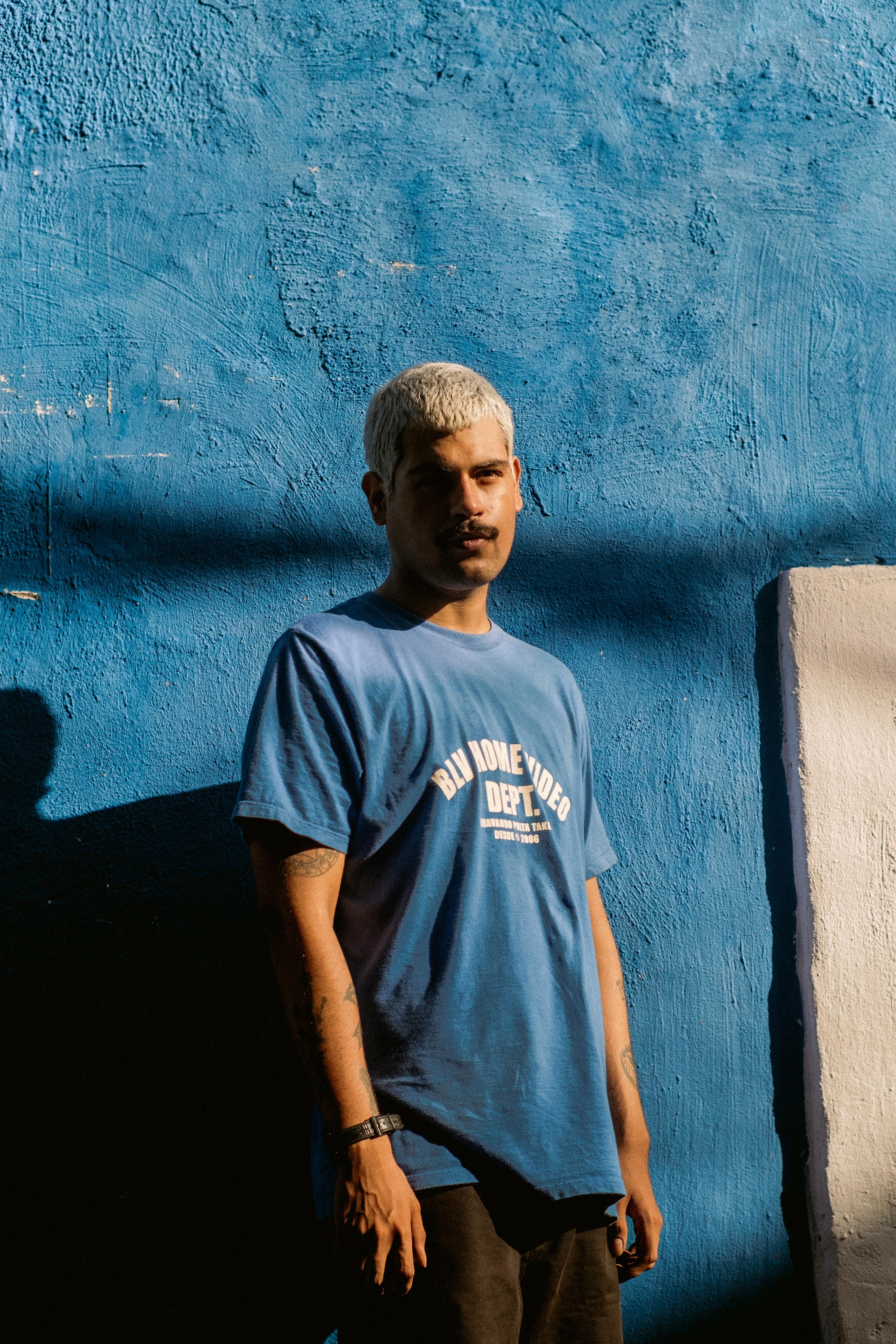 Man standing by a textured blue wall, sunlight casting shadows.