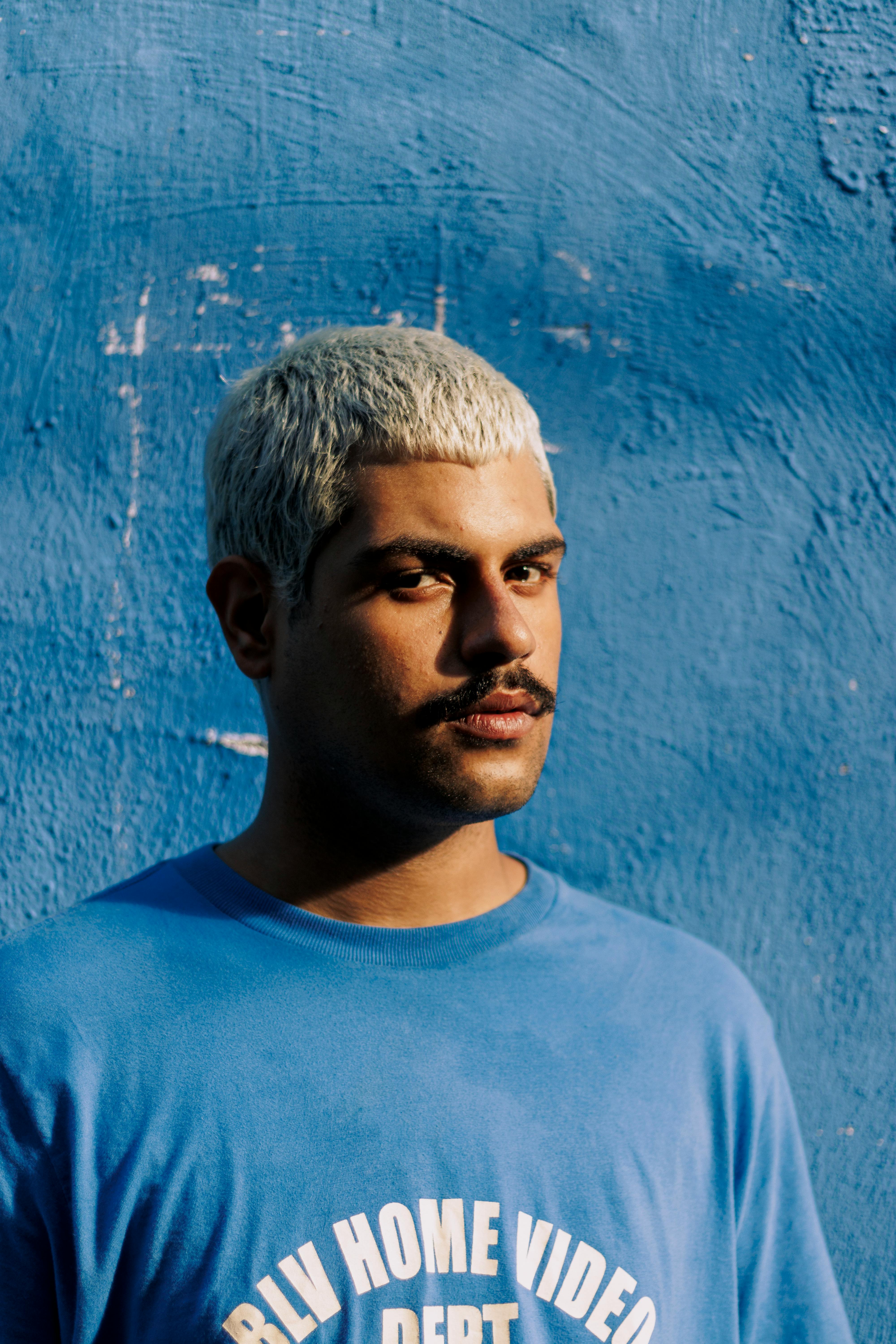 Casual portrait of a young man with bleached hair against a blue wall.