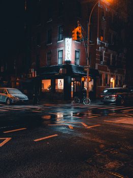 Rain-soaked street at night with glowing neon sign and reflections.