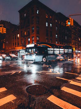 Rainy night city scene with a speeding bus and reflections on wet streets at an urban intersection.