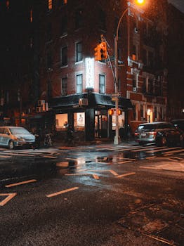 Rain-soaked street corner with a cozy cafe in vibrant city nightscape.