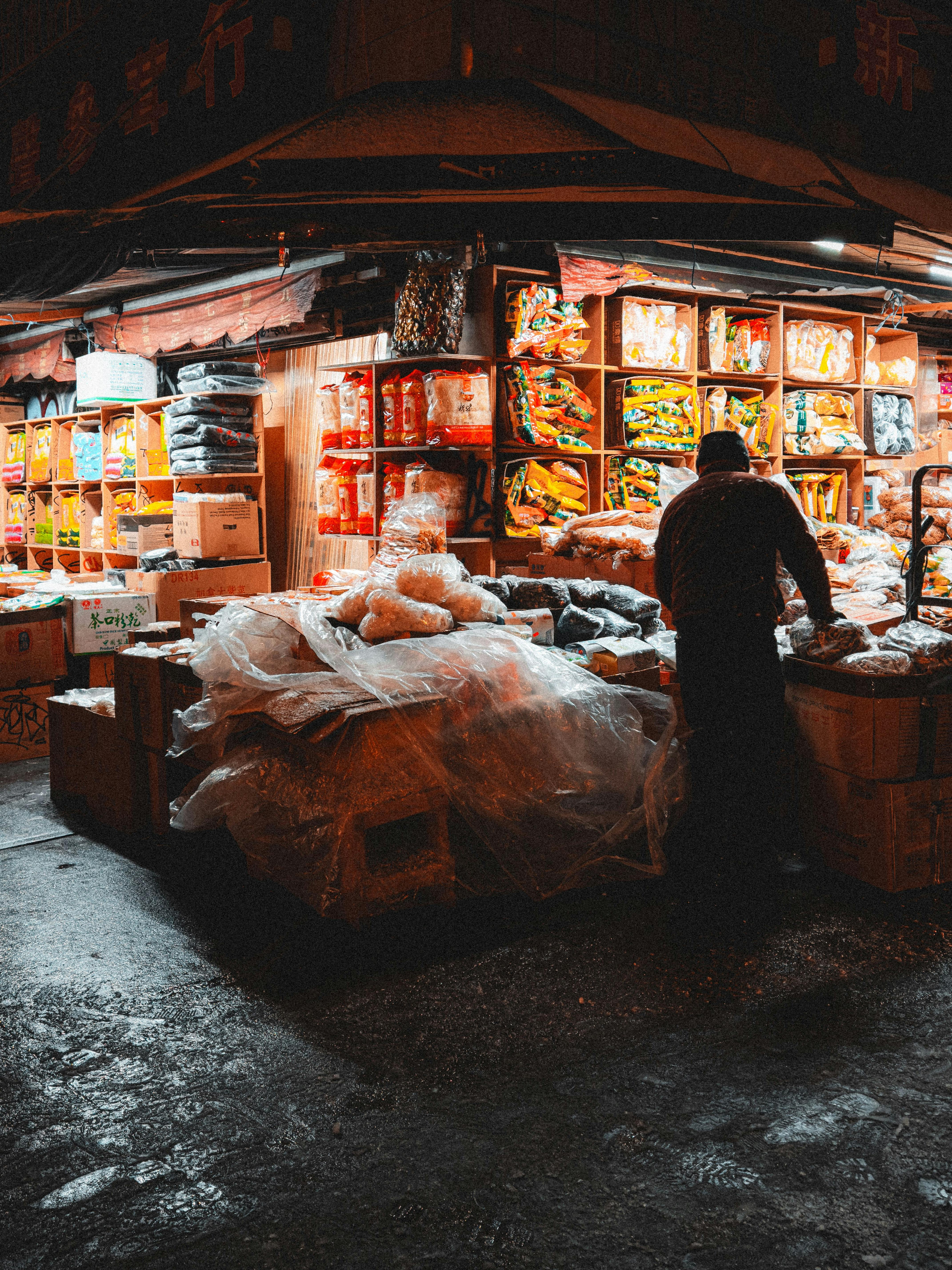 A vibrant market stall at night with colorful packaged goods and street vendor.