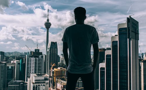 Free Man Standing While Facing Concrete Buildings Stock Photo