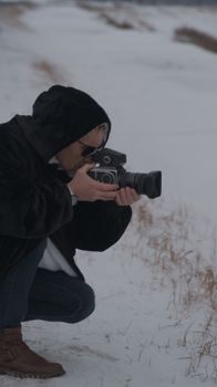 A man in winter clothing uses a vintage camera, capturing nature outdoors.