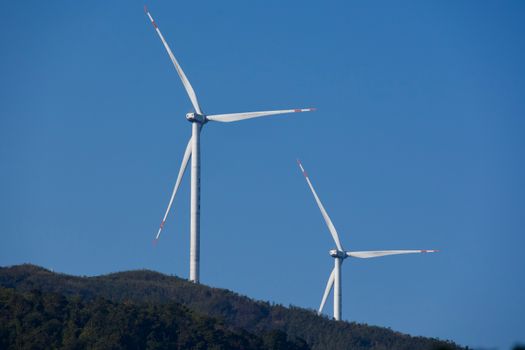 Two wind turbines on a hill with a clear blue sky, representing renewable energy.