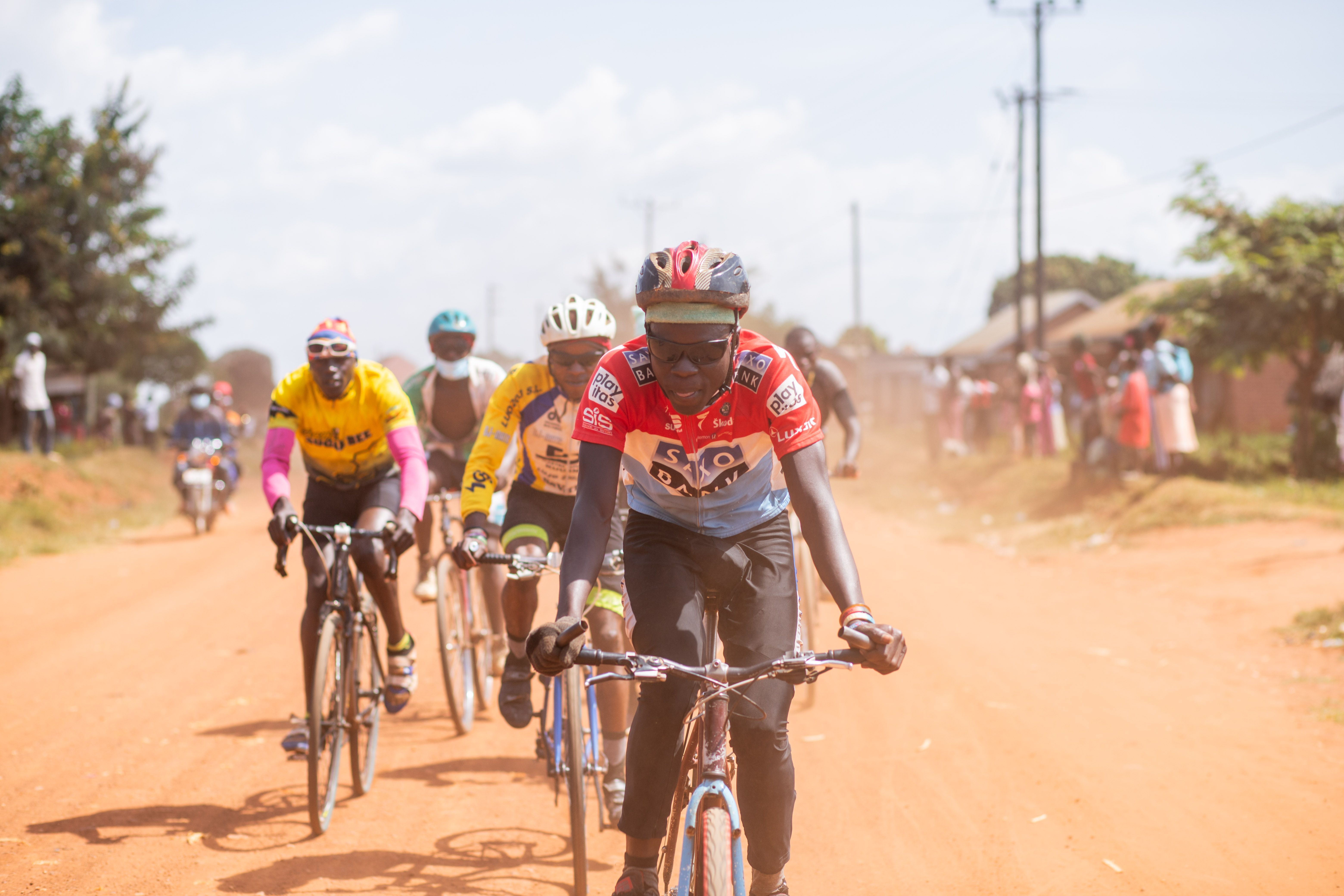 Group of cyclists racing on a dusty road under clear skies during the day.