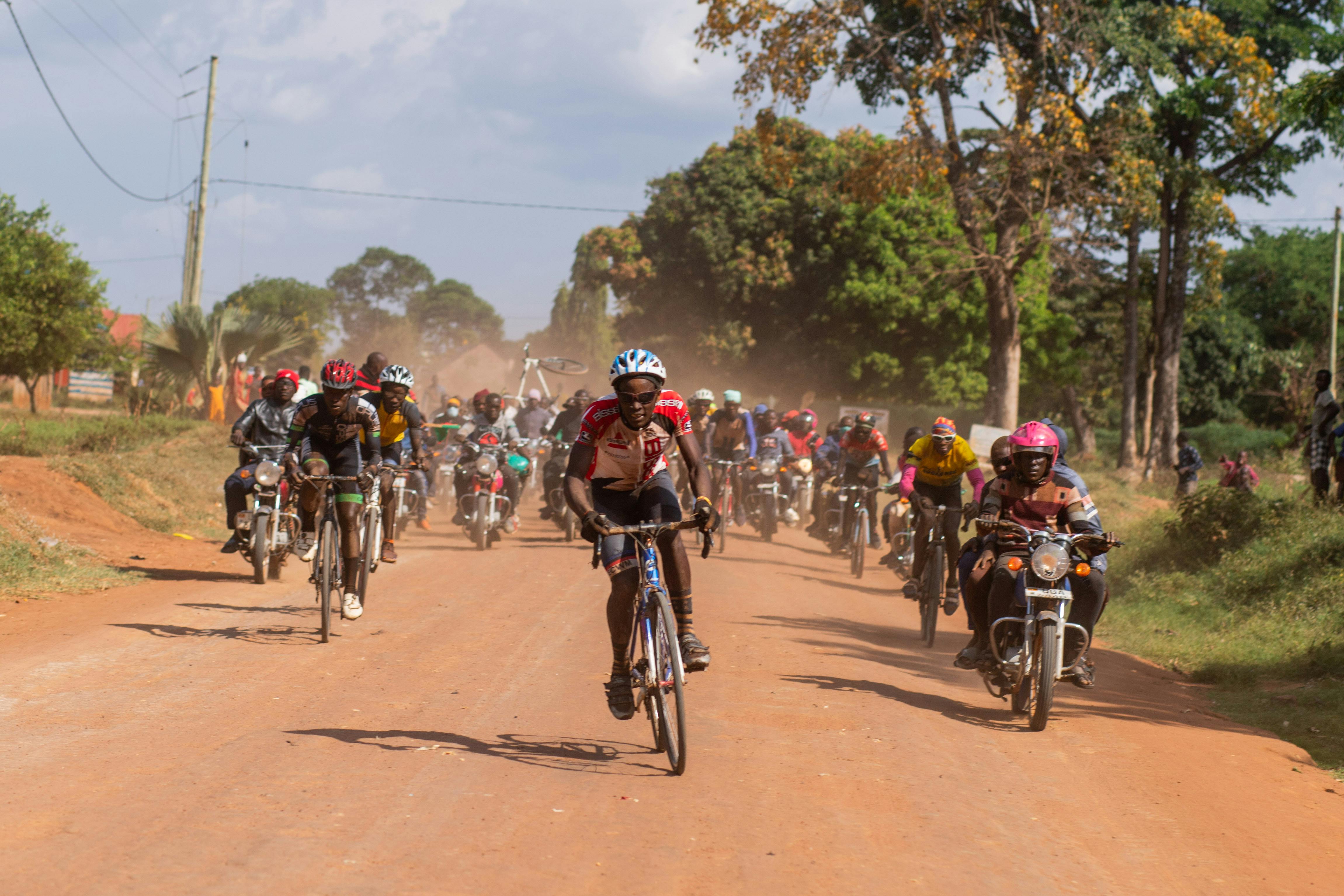 Action-packed scene of cyclists and motorcyclists racing on a rural dirt road.
