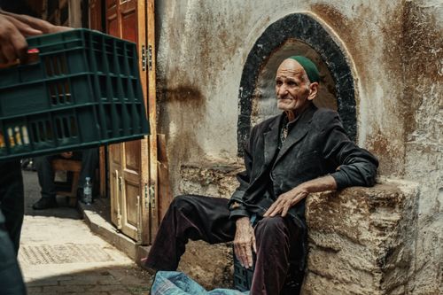 Free A senior man sitting in a Moroccan alleyway, reflecting the cultural and architectural essence of the region. Stock Photo