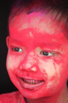 A joyful child with vibrant red paint on their face, celebrating a festival.