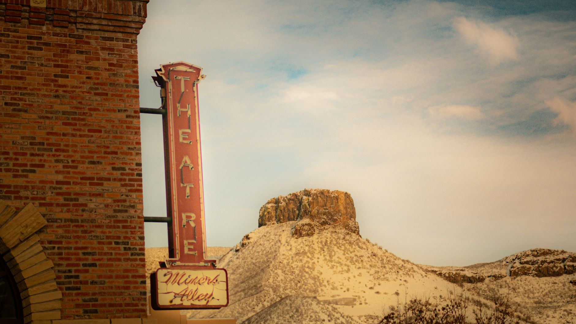 Brick theatre sign with desert hill background under a clear sky.
