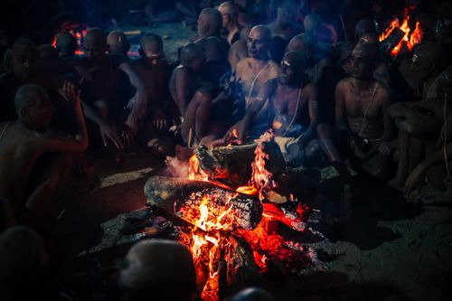 Free A group of adults sitting around a lively campfire at night, creating a communal atmosphere. Stock Photo
