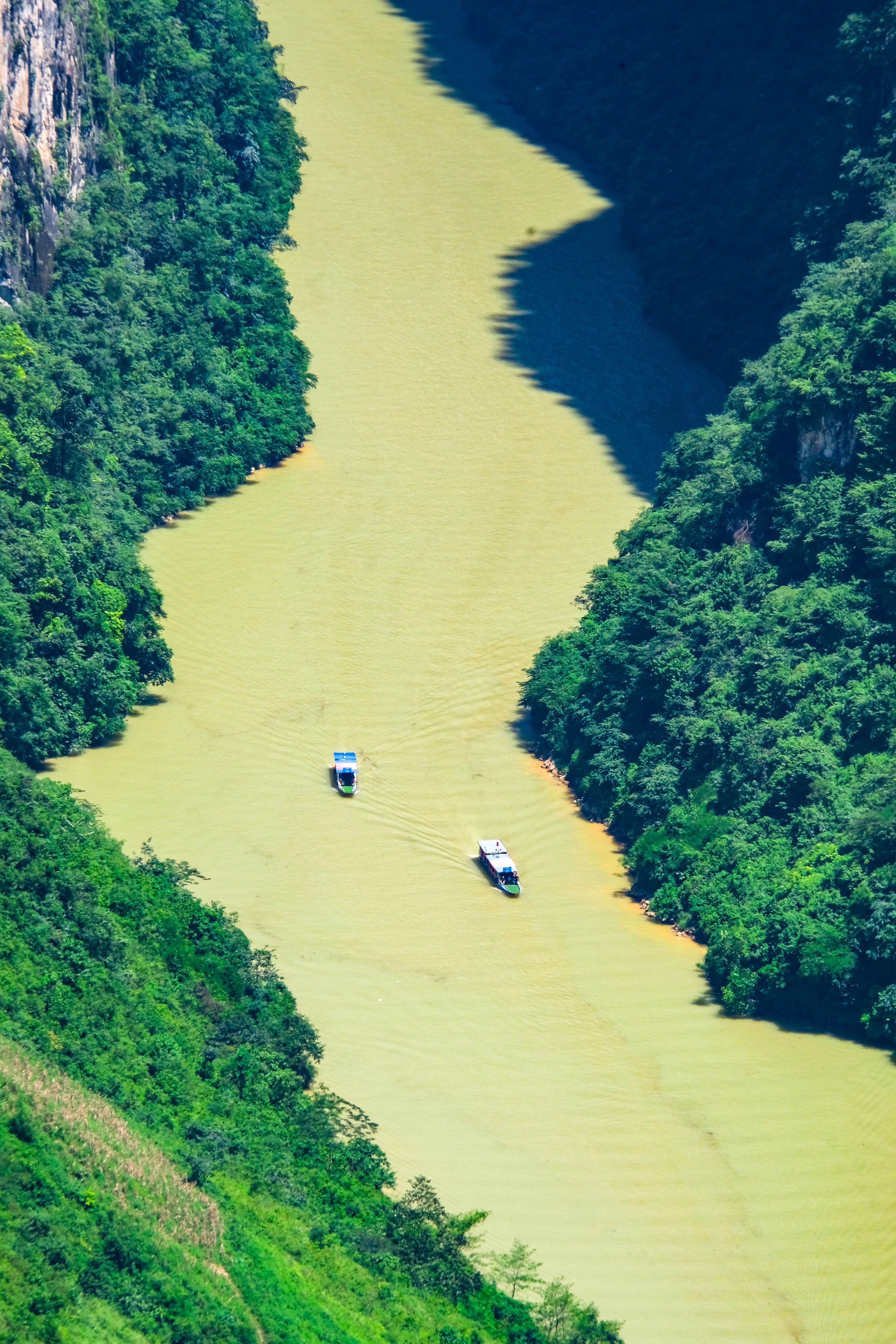 Aerial view of boats navigating a picturesque river surrounded by lush greenery in Hà Giang, Vietnam.