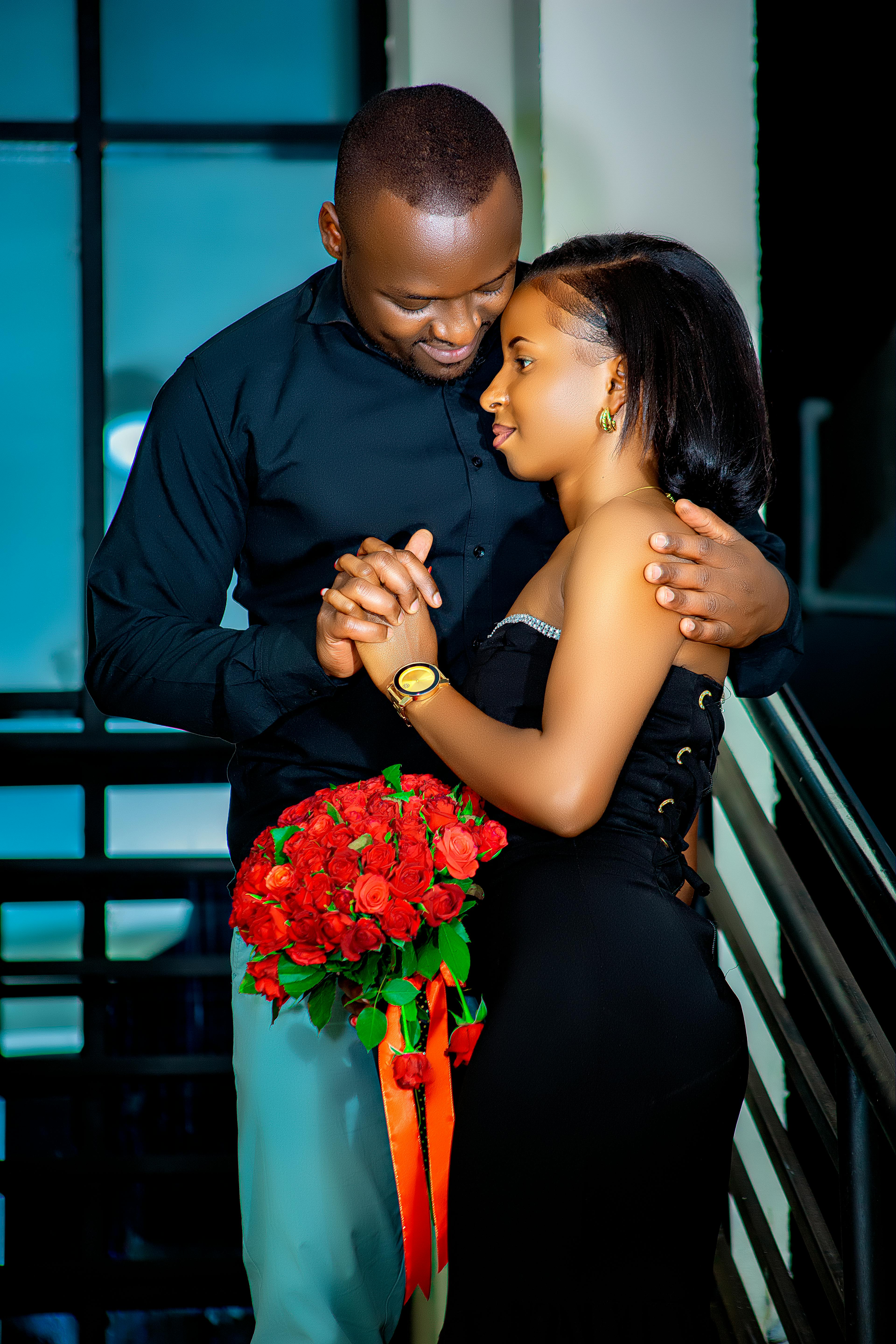 A couple in formal attire holding hands and red roses indoors, exuding love and romance.