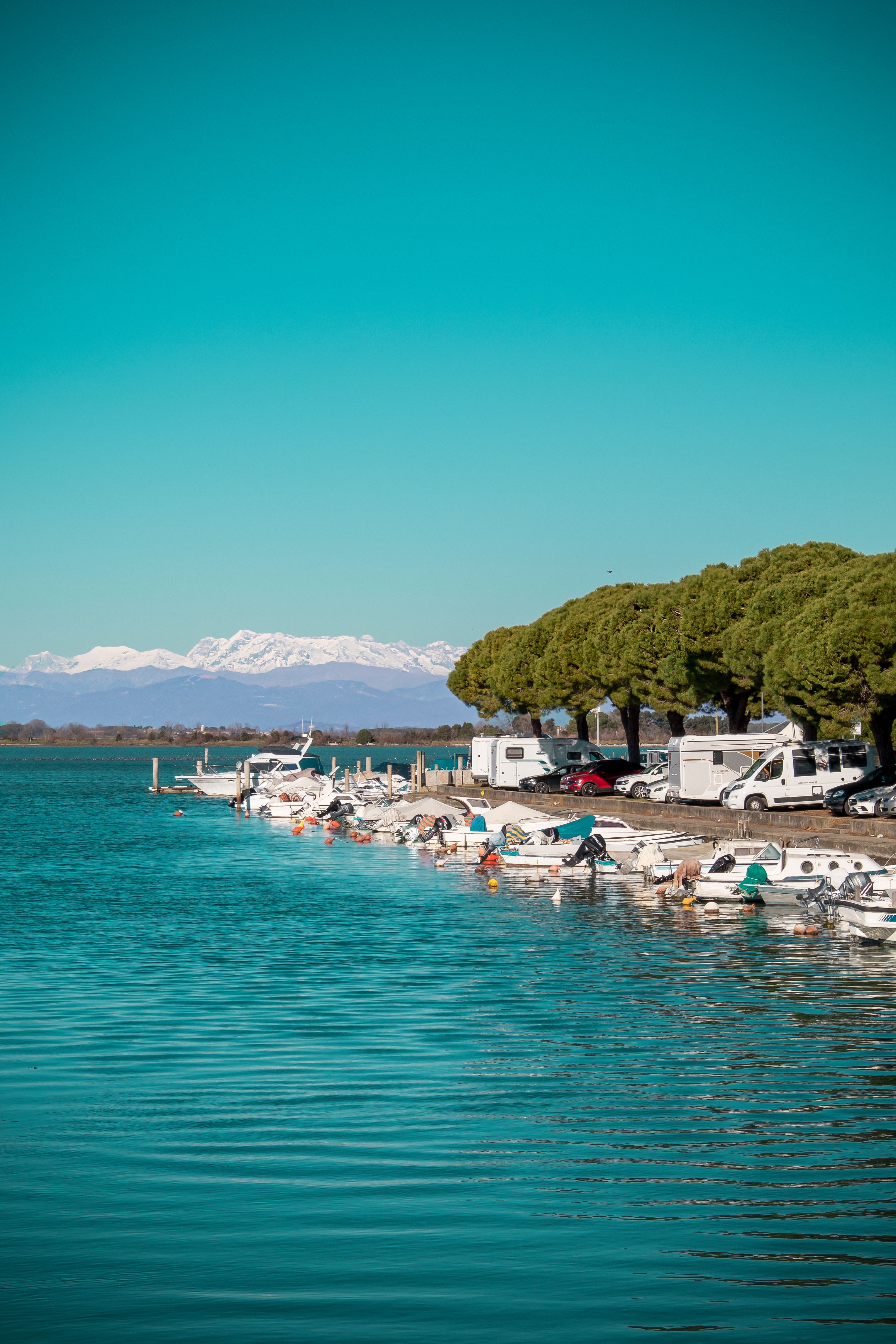 Explore a peaceful lakeside scene with boats, RVs, and mountains in the distance.