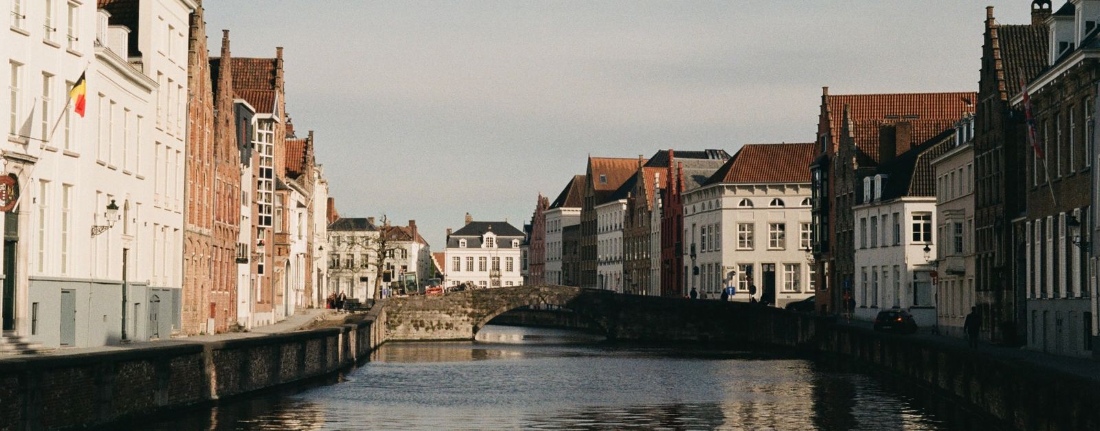 Scenic view of Bruges canal and historic Flemish buildings under clear sky.