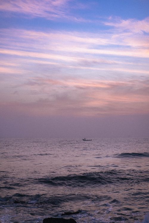 Free Peaceful ocean view at sunset with a small boat on the horizon and vibrant skies. Stock Photo