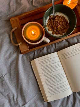 Warm breakfast setup with a bowl of granola, candle, and open book for a relaxing morning.