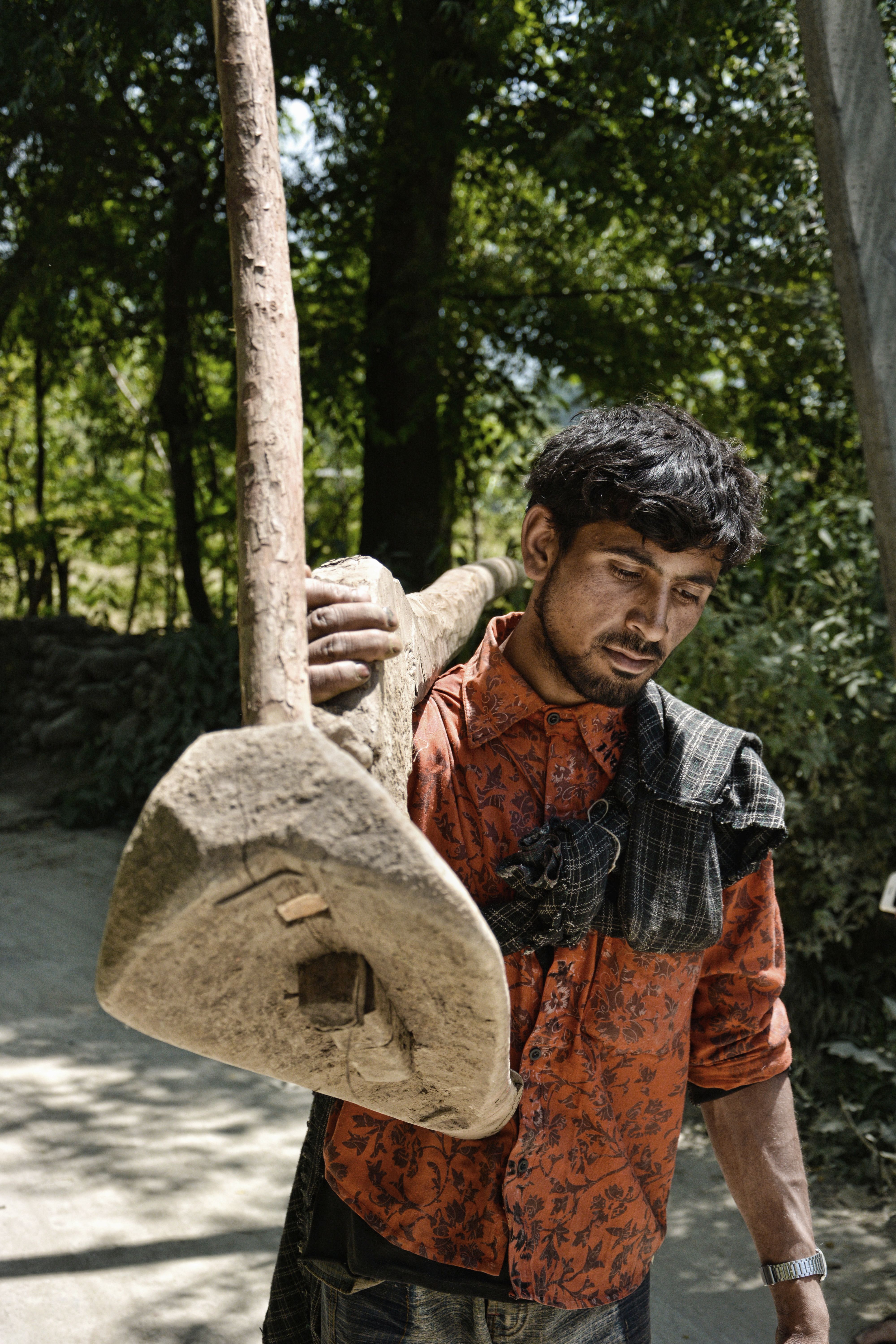 Man carrying a wooden plow in a rural outdoor setting, expression of hard work