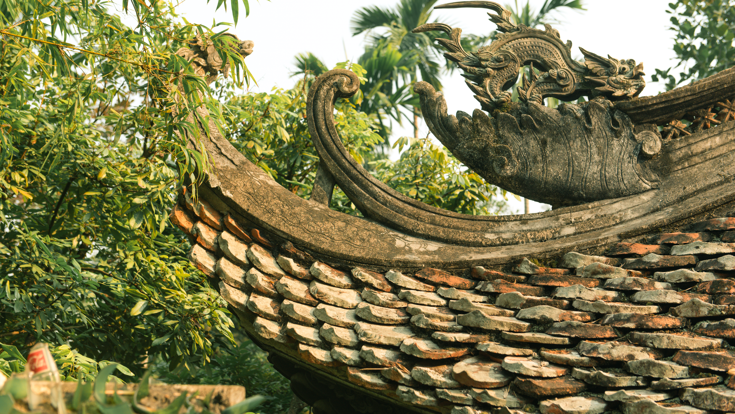 Intricate dragon sculpture on a Vietnamese temple roof surrounded by lush greenery in Hà Nội.