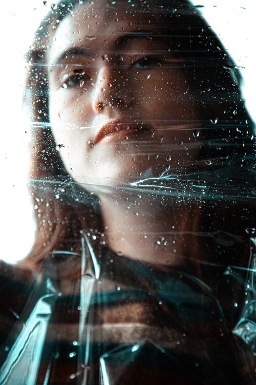 Free Intimate portrait of a young woman looking through a rain-speckled window, capturing a moody atmosphere. Stock Photo