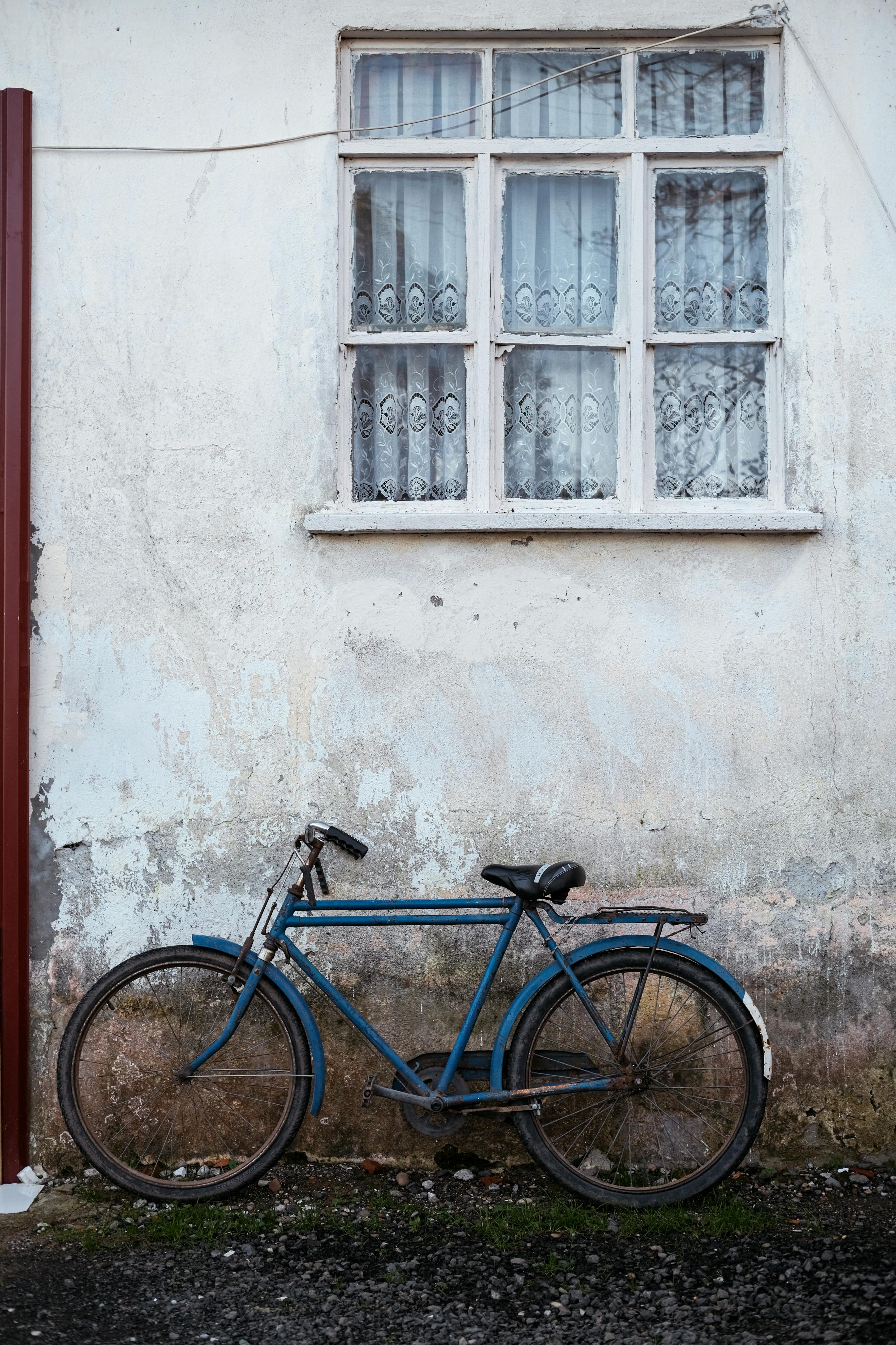 A classic blue bicycle rests against a textured wall beneath a window in Türkiye.