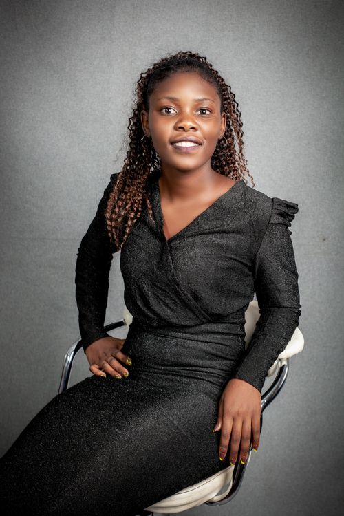 Free Portrait of an African woman smiling elegantly in a black dress, seated indoors. Stock Photo