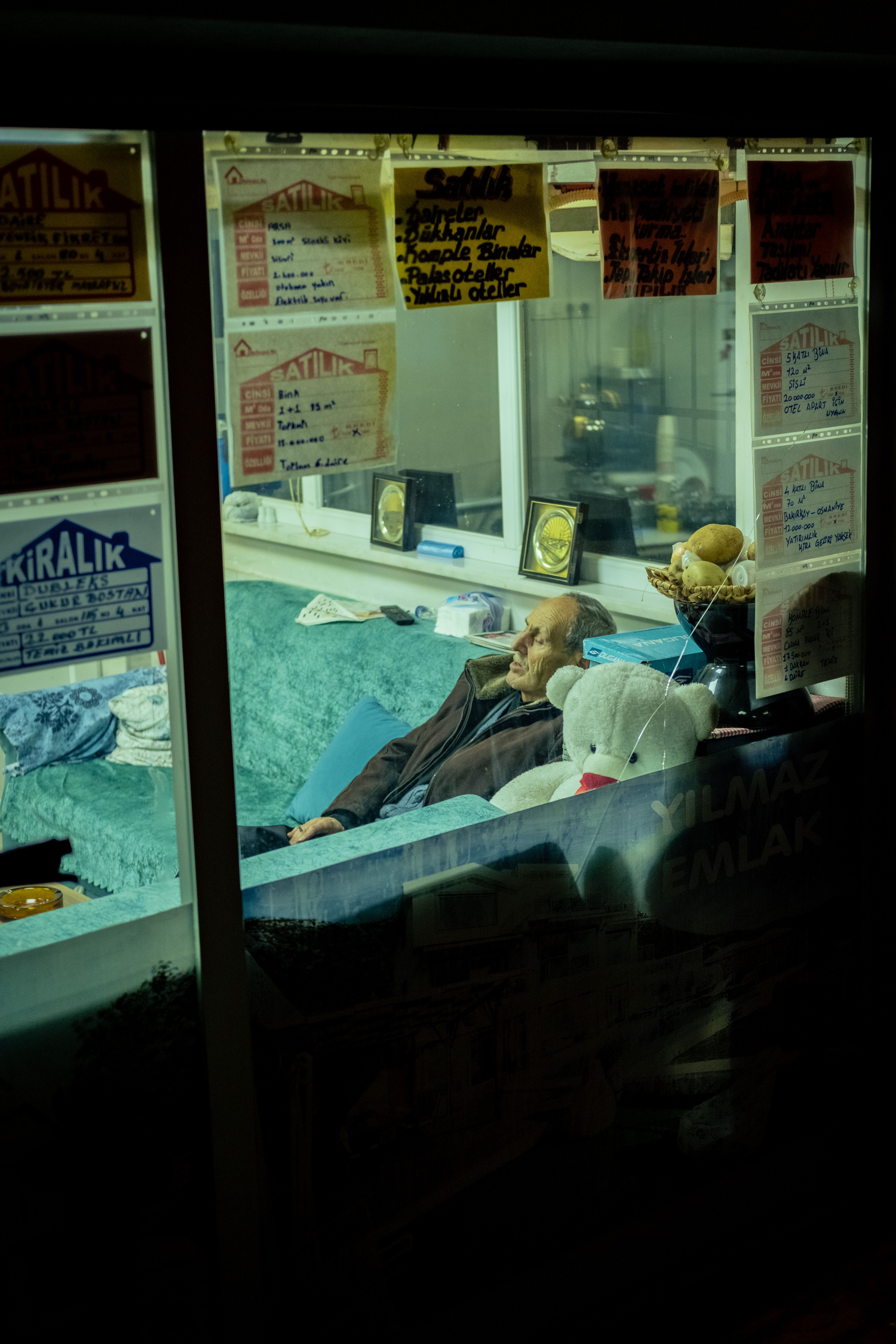 An adult man resting in an office with rental signs in the window, photographed at night.