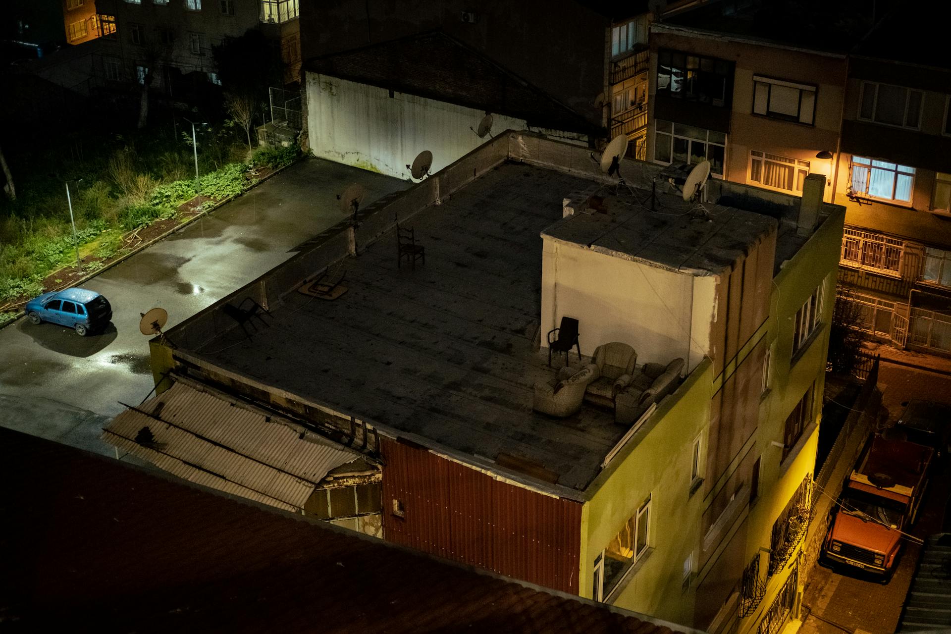 Aerial view of an urban rooftop at night with chairs and satellite dishes.